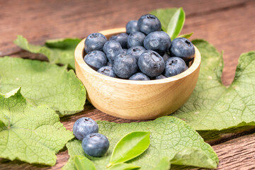 Fresh Blueberries on wooden tray with green leaves background.