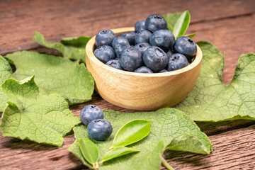 Fresh Blueberries on wooden tray with green leaves background.