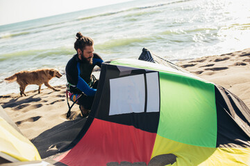 Young man professional surfer standing on the sandy beach with his kite
