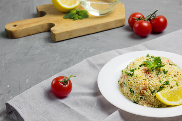 Traditional Arabic salad or Tabbouleh on white plate, healthy vegetarian dish with couscous on cement background