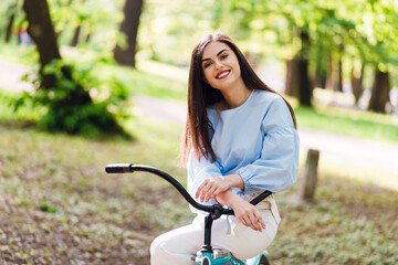 Obraz premium Adorable woman sitting on retro blue bicycle at park