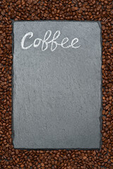 Background or texture made of roasted brown coffee beans and stone serving board with chalk handwritten sign
