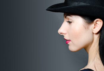 Portrait of a beautiful young woman in a hat on a black background, closeup, side view