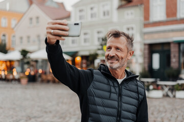 Tourist holding up his mobile phone taking a selfie in a town