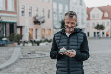 Middle-aged trendy man using his mobile phone in a deserted town square