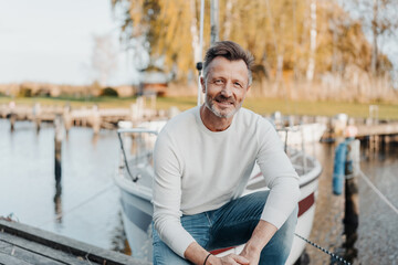 Relaxed attractive man squatting on a jetty in front of his yacht