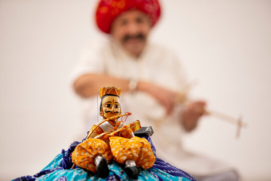 A HANDMADE KATHPUTLI KEPT IN FRONT OF CAMERA WITH THE ARTIST IN BACKGROUND	