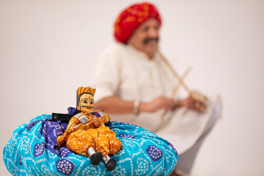 A TRADITIONAL KATHPUTLI KEPT IN FRONT OF CAMERA WITH THE ARTIST IN BACKGROUND	