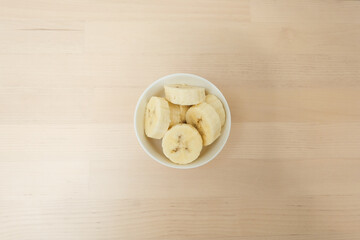 Fresh ripe organic sliced bananas in a ceramic bowl on a wooden table on top view