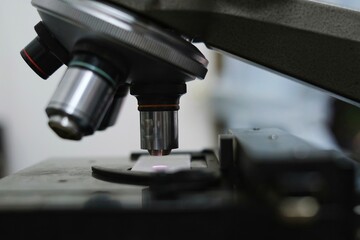 A close up picture of objective lens and stage of a microscope made from metal and glass in a laboratory.