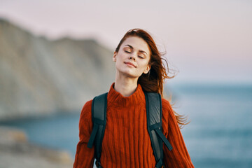 woman in a red sweater with a backpack on her back resting in the mountains outdoors near the ocean 