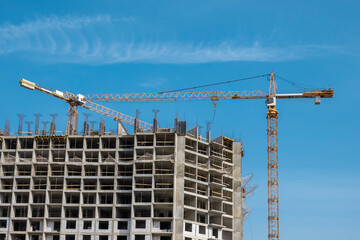 Two construction cranes against a blue sky background. Construction tower crane in yellow colour....