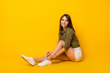 Photo of young lady sit floor tie shoelace wear green shirt short skirt sneakers isolated yellow...