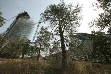 Construction site of modern high-rise ski-jump in Shchuchinsk city, Kazakhstan. Crane and scaffoldings down-up view. Pine-trees around. Wide-angle lens.