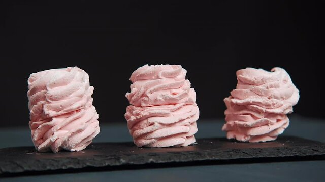 Close up panorama view on three pink zephyr cookies served on black. Marshmallow or zephyr - sweet strawberry fruit taste. Slow motion view of a dessert over black.