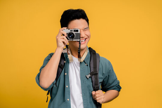 Portrait of a young backpacker Asian tourist taking a picture on a yellow background. He is very happy.