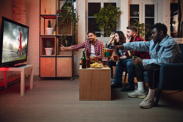 Group of friends watching TV, sport match together. Emotional fans cheering for favourite team, watching on exciting game. Concept of friendship, leisure activity, emotions