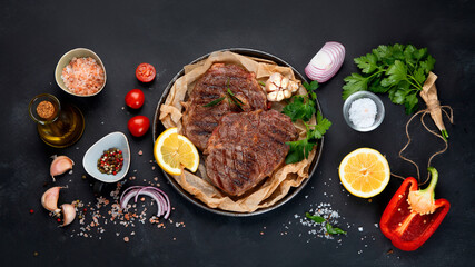 Delicious prepared meat steaks with seasoning and herbs on dark background.