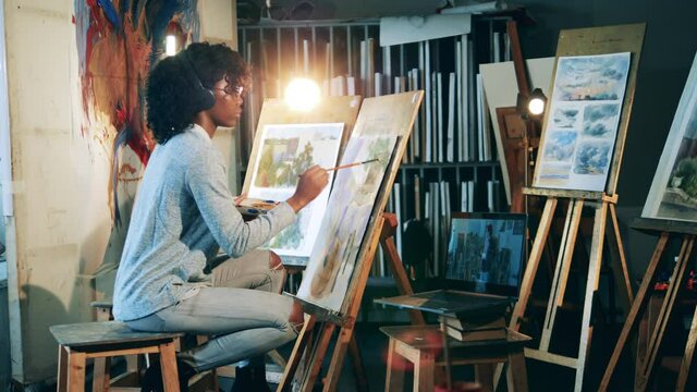 African ethnicity woman in headphones is painting a picture