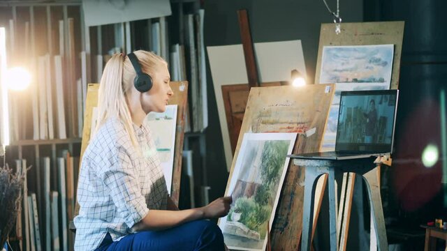 Blond lady is using a video lesson to learn painting
