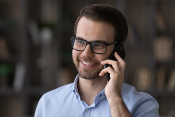 Close up of smiling young Caucasian man in glasses look in distance talk speak on cellphone call. Happy millennial male have pleasant smartphone conversation online. Communication concept.
