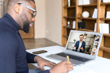 African man takes part in an online strategic meeting with mentor to build business or his brand, writing down in notebook ways of business development or problem solving, using fast convenient app - obrazy, fototapety, plakaty