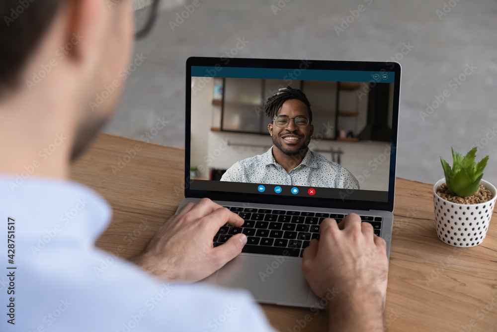 Wall mural close up back view of man use laptop talk on video call with smiling african american business partn