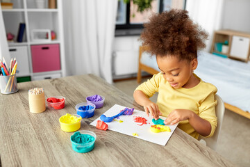 childhood, creativity and hobby concept - little african american girl with modeling clay playing at home