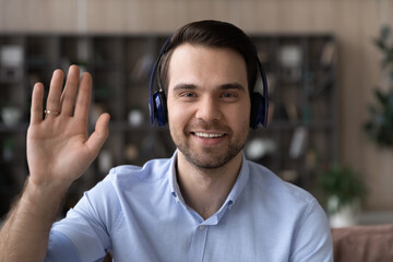 Headshot portrait of smiling young Caucasian man in headphones talk speak on video call on computer...