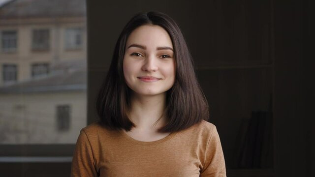 Portrait of caucasian millennial cute attractive woman looks into camera nodding her head, expressing agreement approval, answering yes. Close-up brunette girl teenager posing at home indoors smiling
