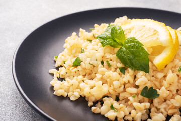 Boiled bulgur with fresh lemon and mint on a plate. A traditional oriental dish called Tabouleh. Gray concrete background