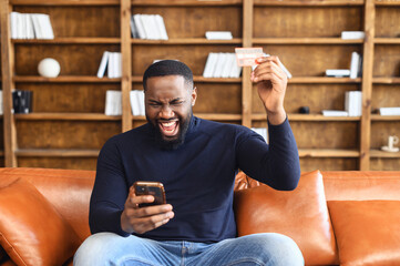 Happy hilarious young multiracial man involved in online shopping, celebrating getting gift or...