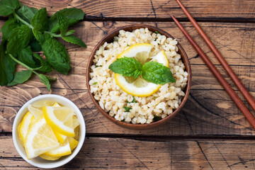 Boiled bulgur with fresh lemon and mint on a plate. A traditional oriental dish called Tabouleh. wooden background rustic top view, copy space