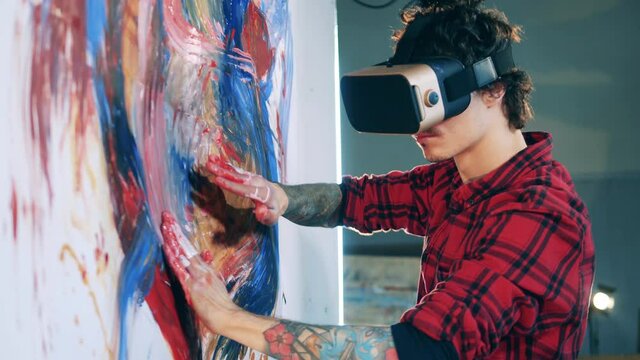 An artist in VR-glasses is painting a colourful picture. Virtual reality, futuristic art concept.