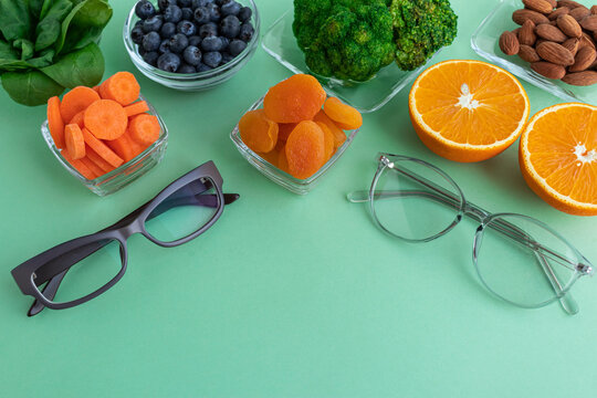 Two glasses and products for improving vision, spinach, dried apricots, blueberries, orange, almonds and broccoli on a green background.