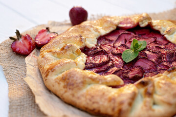 Freshly baked homemade galette or open strawberry pie and fresh mint leaves, summer food. Soft selective focus.