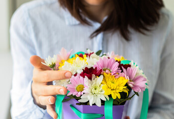 Young woman holding beautiful purple basket full of colorful flowers in her hands. Celebration, birthday or every day gift.