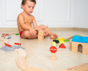 Child playing with wooden toys on the floor of his room, in summer.