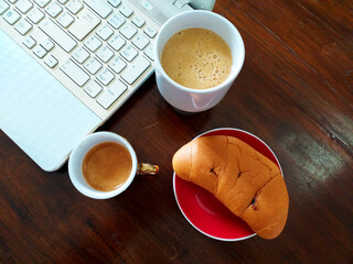 Foto concettuale di Smart working in orario da colazione, con computer accanto al caffè, il succo di frutta e il cornetto ripieno al cioccolato