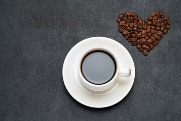 Cup of espresso and Heart shaped roasted coffee beans on dark concrete background