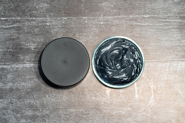 Homemade face mask and scrub with activated carbon powder and yogurt on wooden background with jar packaging