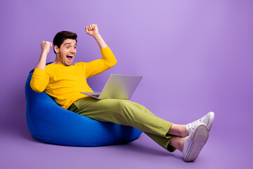 Photo of young happy crazy excited smiling man sit armchair with laptop raise fists in victory...
