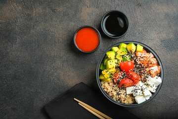 Poke bowl with quinoa, salmon, avocado and feta cheese on a dark background top view with copy space. Home delivery food.