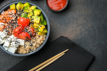 Poke bowl with quinoa, salmon, avocado and feta cheese on a dark background top view with copy space. Home delivery food.