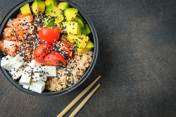Poke bowl with quinoa, salmon, avocado and feta cheese on a dark background top view with copy space. Home delivery food.