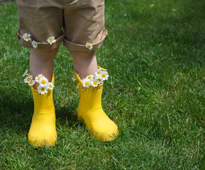 baby boy's legs in bright yellow boots and brown shorts. Daisy flowers stick out from the boots. Humor and positive concept. The joy of childhood. Mother's day gift