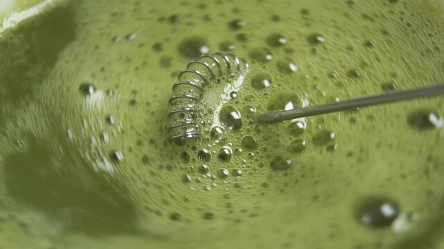Swirl matcha green tea and froth with electro spiral frother in slow motion. Macro shot. Traditional Japanese natural drink
