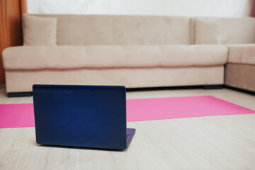 Online workout at home. Laptop on the yoga mat on floor in living room in modern apartment interior. 