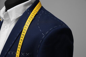Semi-ready jacket with tailor's measuring tape on mannequin against grey background, closeup - obrazy, fototapety, plakaty