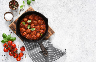 Meat balls with tomato sauce in a frying pan on a light concrete background.